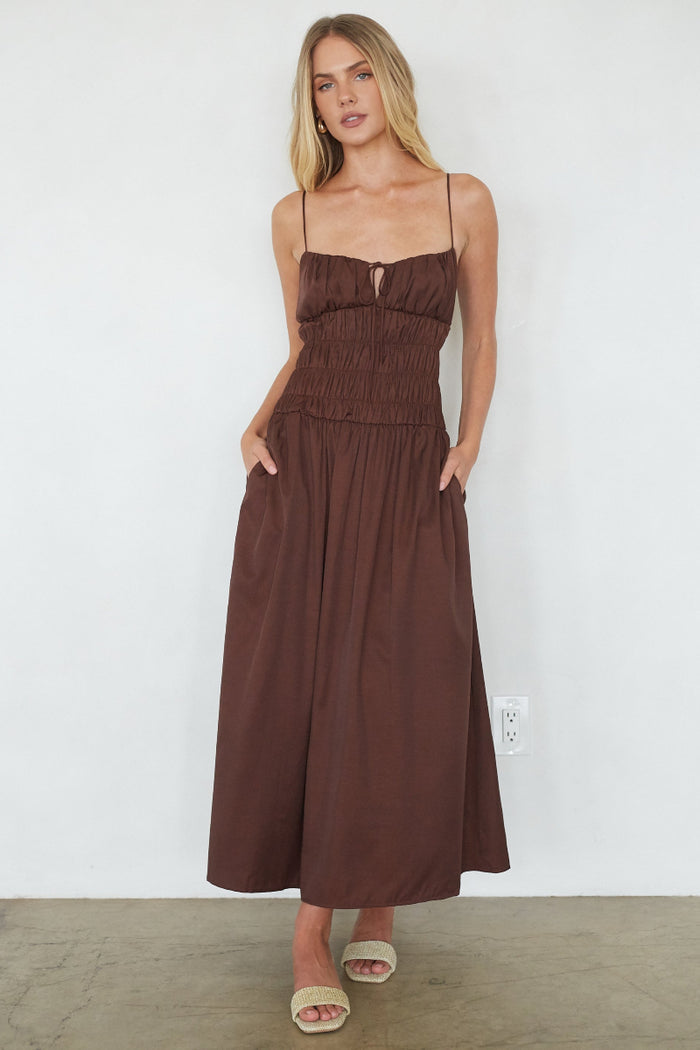 brown-image | Woman wearing a brown dress standing against a white wall.