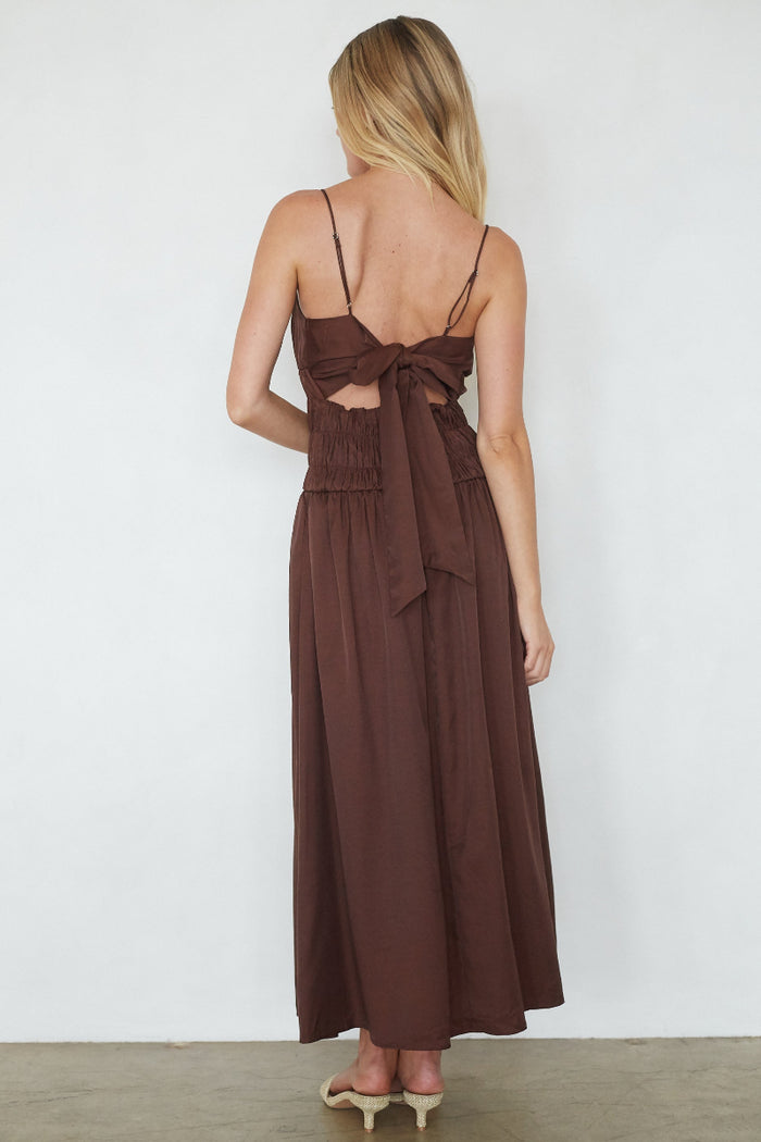 Woman wearing a brown dress with cut-out back and bow detail on a white background