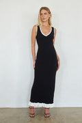Woman wearing a black sleeveless dress with white trim against a plain background