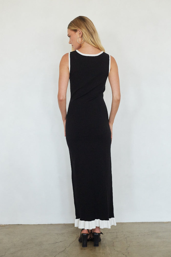 Woman wearing a black dress with white ruffled hem against a white background