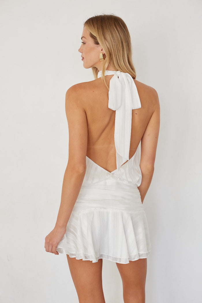 Woman wearing a white dress with a bow detail on the back against a plain background