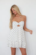 Woman wearing a white strapless dress with black polka dots on a plain background