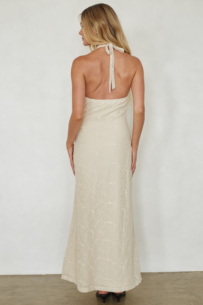 Woman wearing a long, light-colored dress with thin straps against a white background