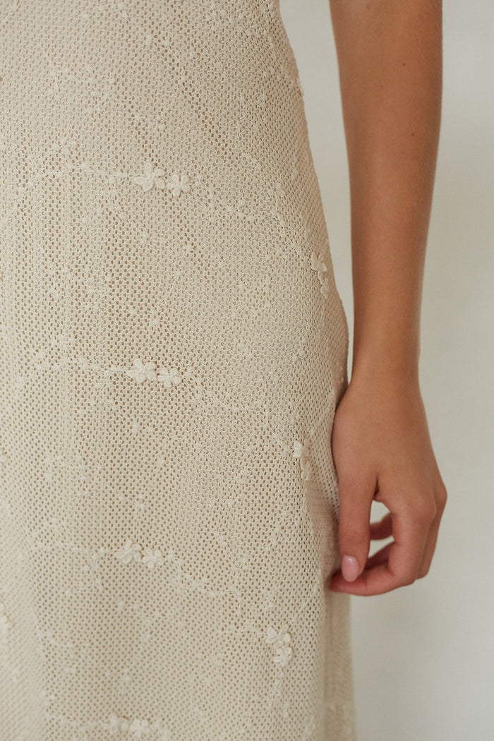 Beige lace dress with a hand visible at the bottom right corner on a plain background