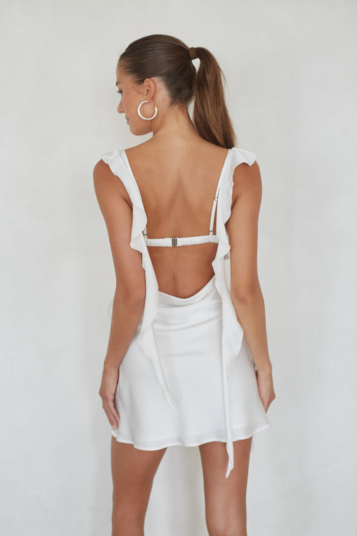 Woman wearing a white dress with cut-out back design on a plain background