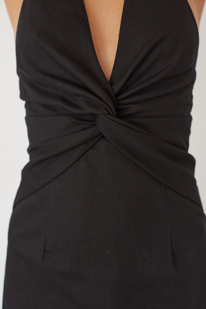 Black dress with a deep neckline and knot detail on a light gray background