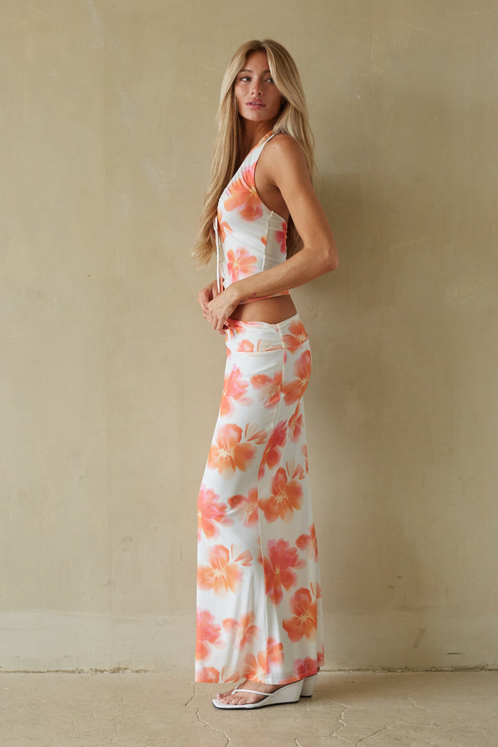 Woman wearing a floral dress standing against a beige wall.