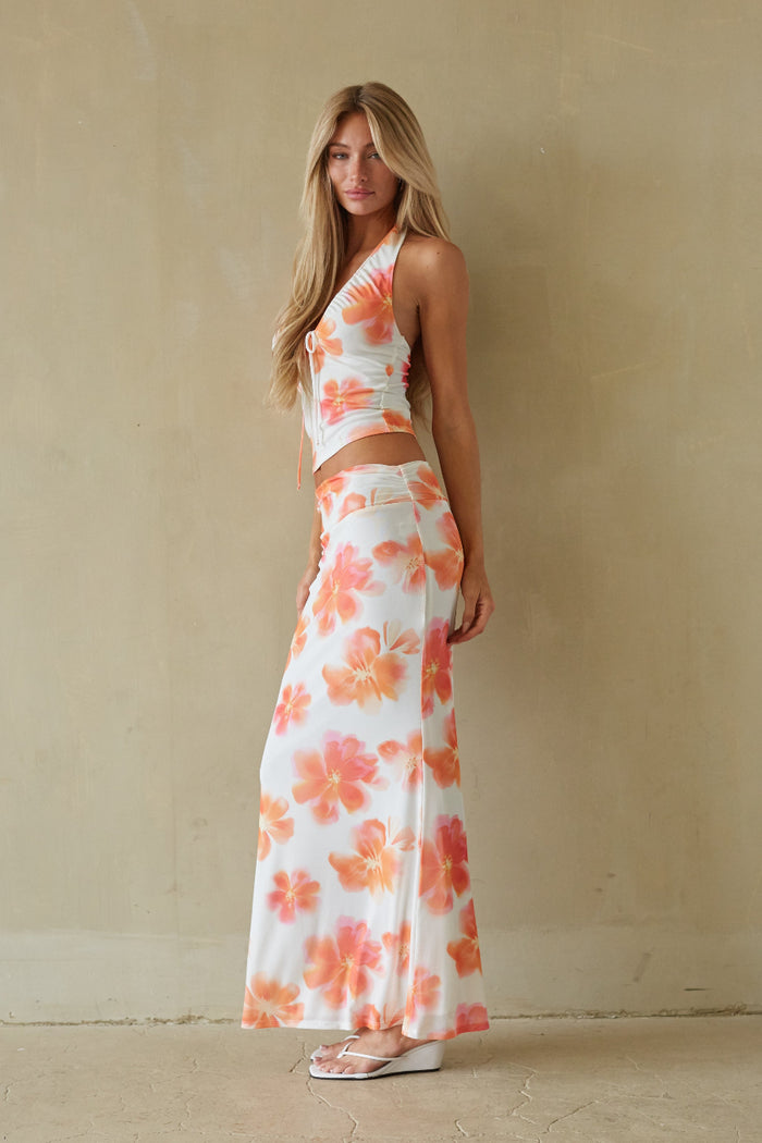 Woman wearing a floral two-piece outfit against a beige wall.