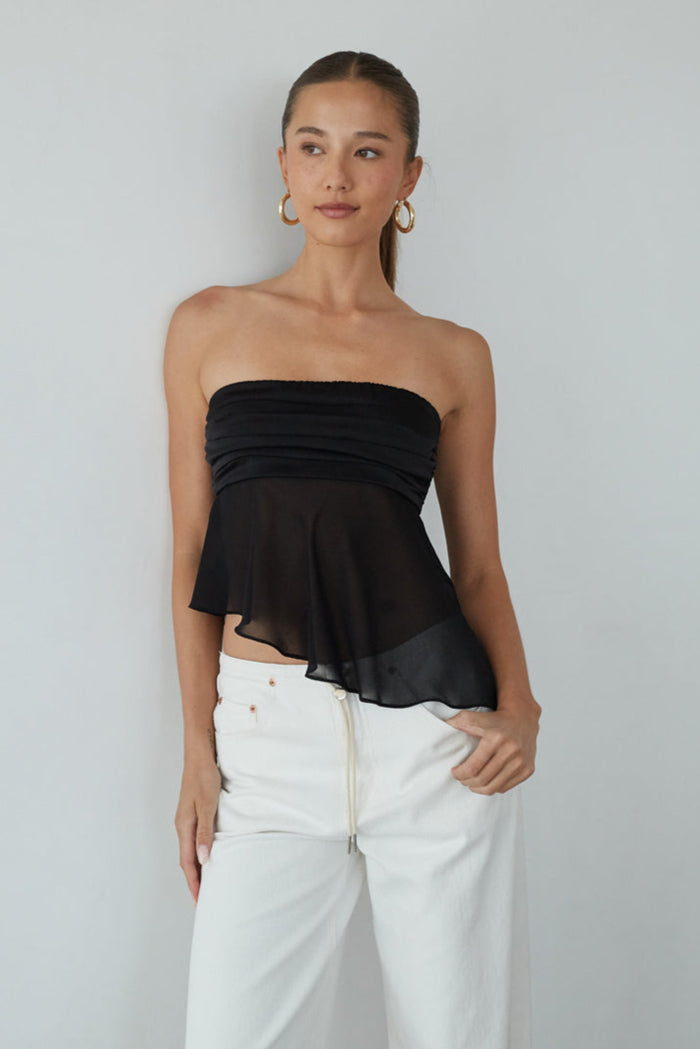 Woman wearing a black strapless top and white pants against a plain background