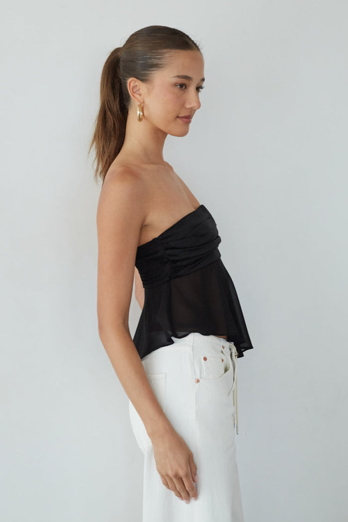 Woman wearing a black strapless top and white pants against a plain background