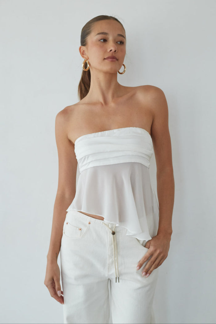 Woman wearing a white strapless top and white pants against a plain background