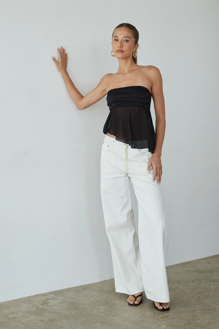 Woman wearing a black strapless top and white pants against a plain background