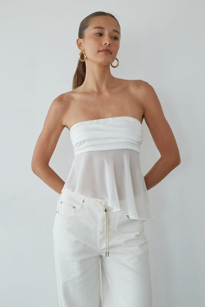 Woman wearing a strapless white top and white pants against a plain background