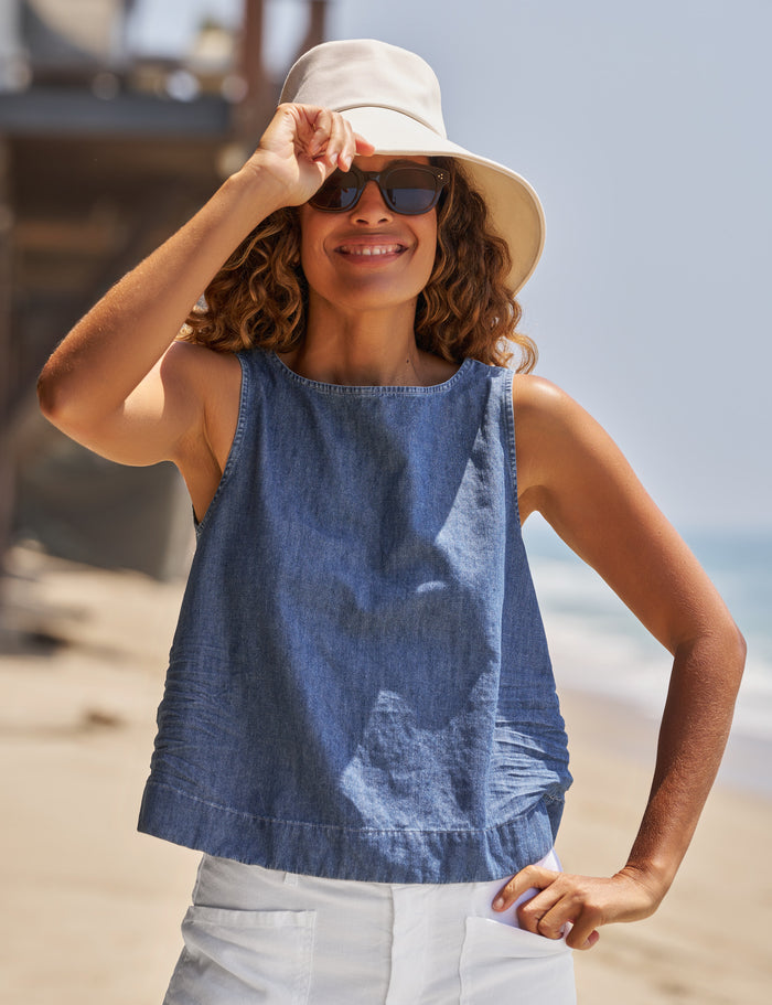 Woman wearing a blue sleeveless top and beige hat on a beach.