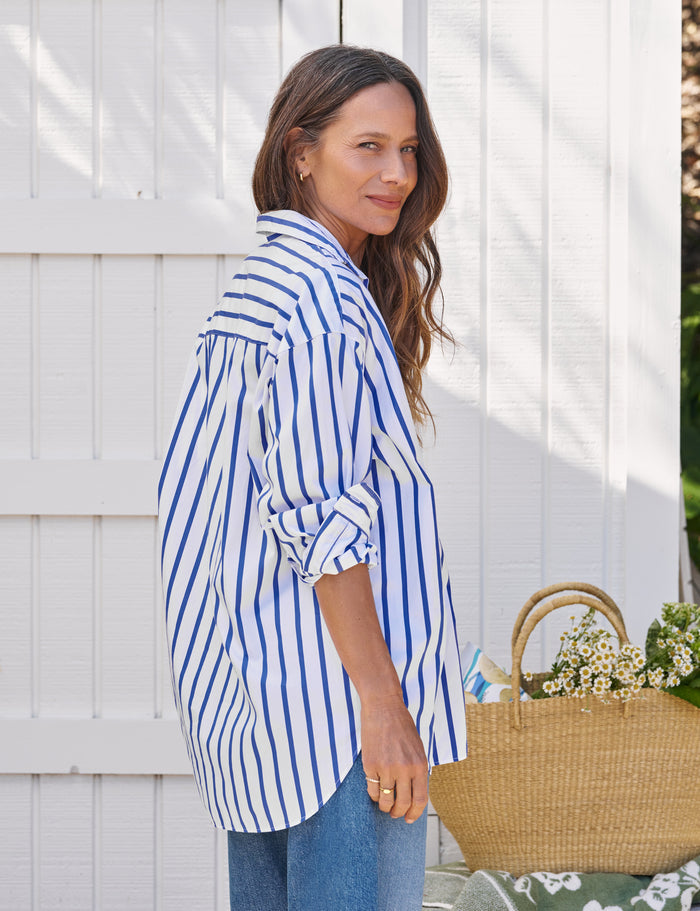 Woman wearing a blue and white striped shirt with rolled-up sleeves, standing next to a white fence.