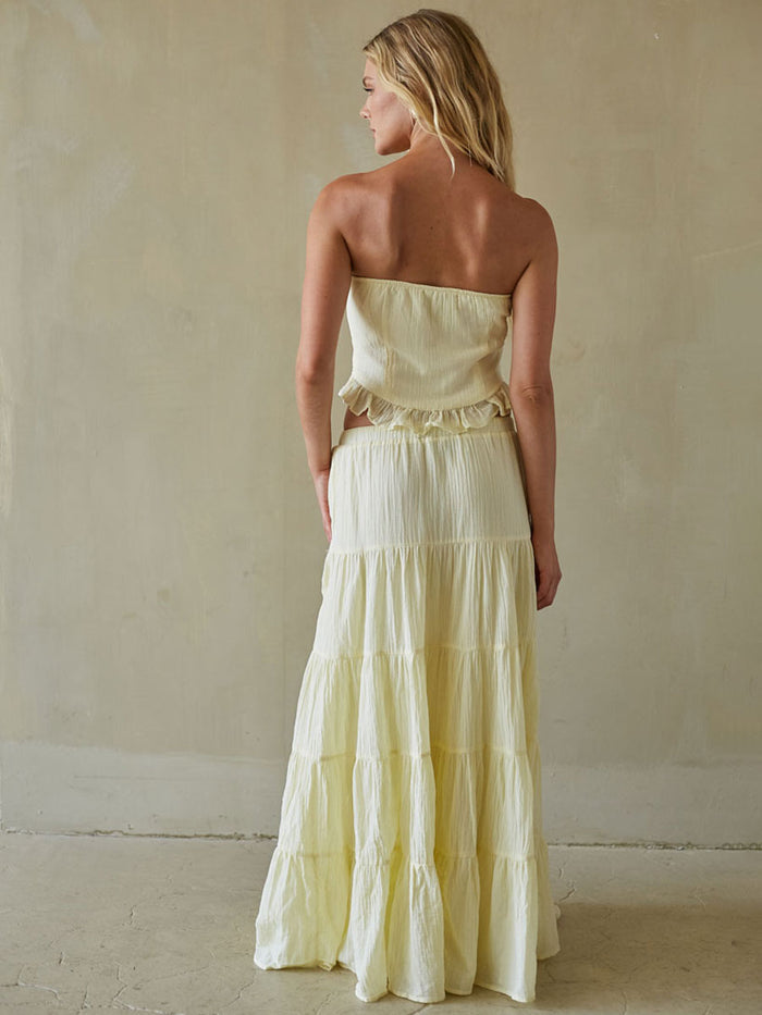 Woman wearing a strapless, tiered yellow dress against a plain background