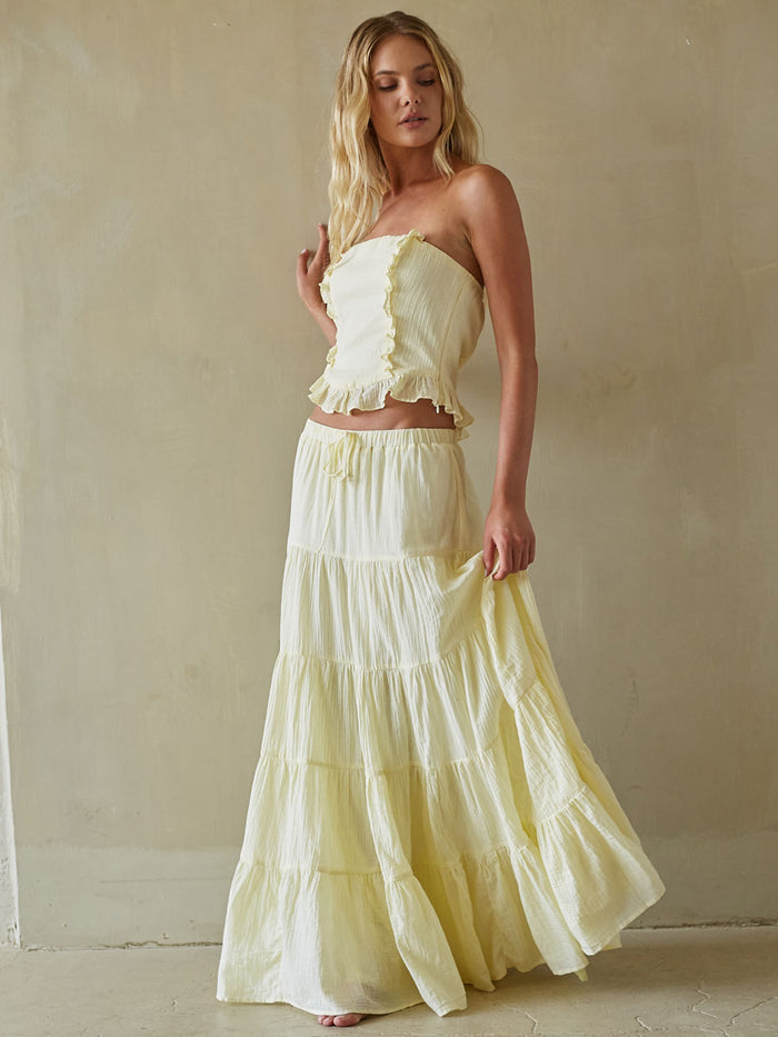 Woman wearing a light yellow strapless top and tiered skirt against a neutral background