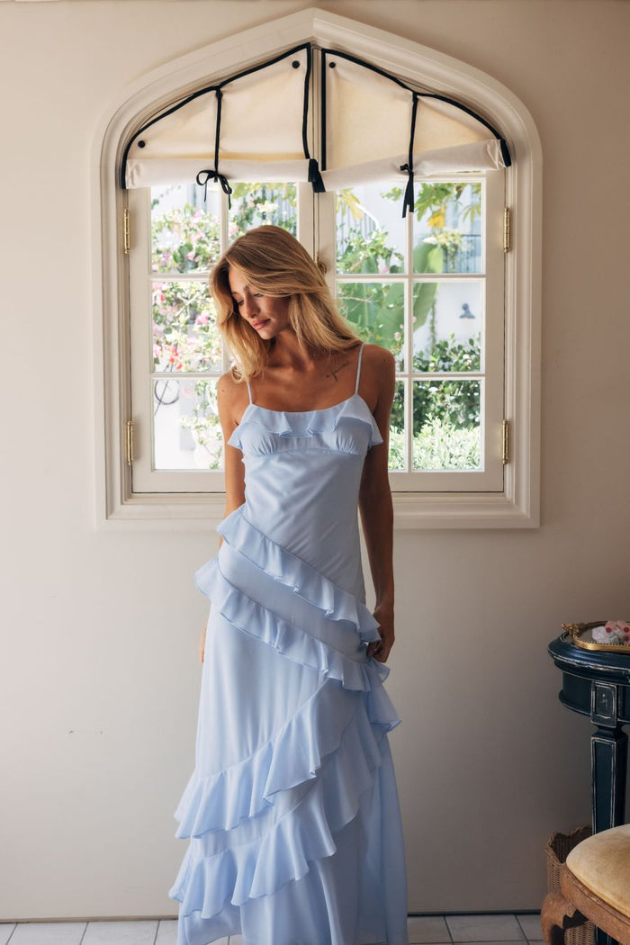 Woman in a light blue ruffled dress standing in a room with a large window.