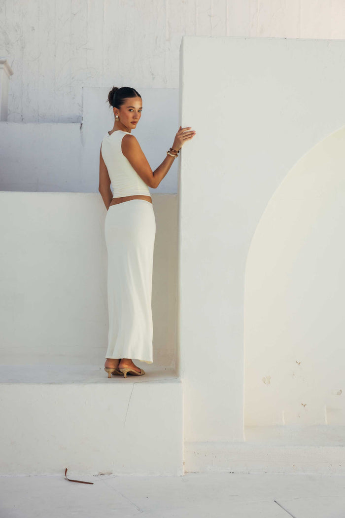 Woman in a white outfit standing against a white wall with architectural elements.