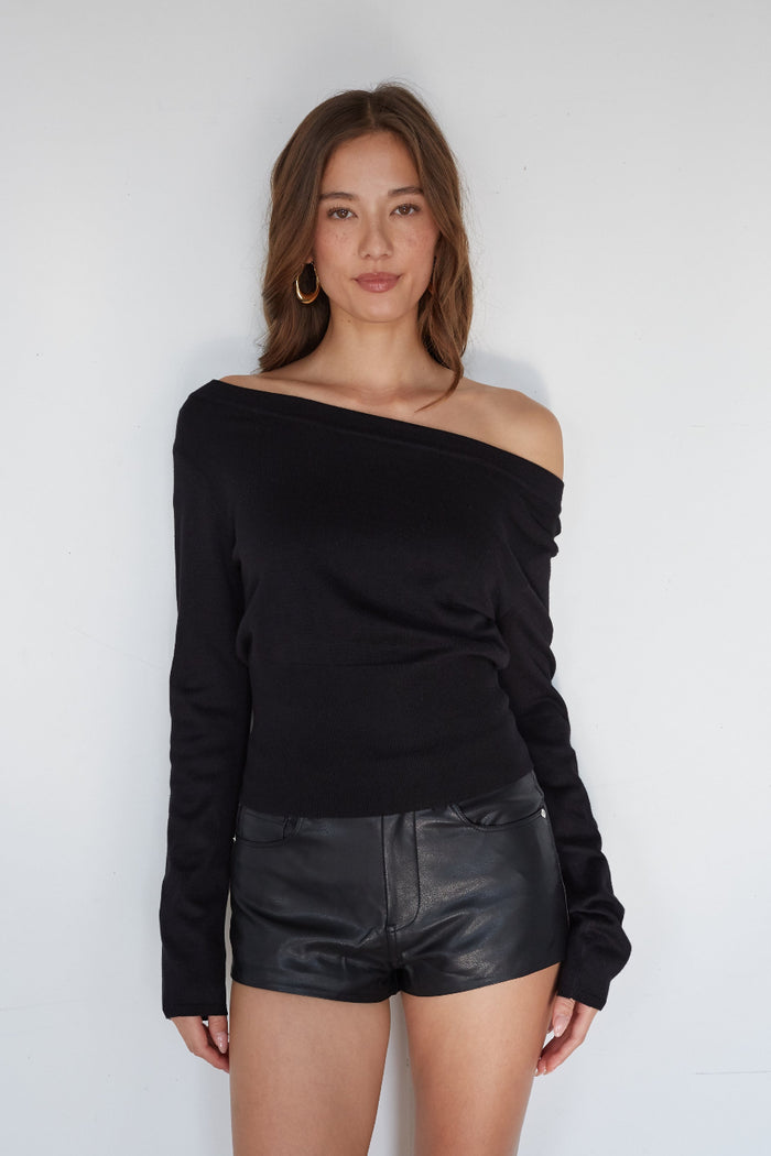 Woman wearing a black off-shoulder top and leather shorts against a white background