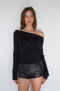 Woman wearing a black off-shoulder top and leather shorts against a white background