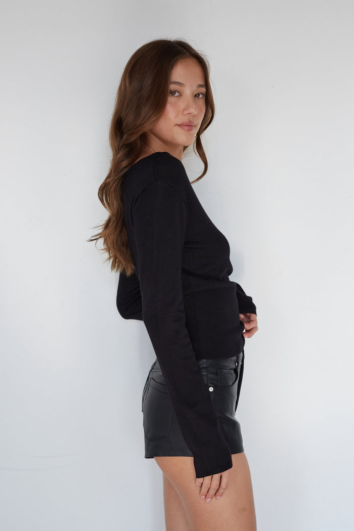 Woman wearing a black long-sleeve top and black leather skirt against a white background