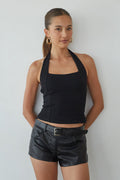 Woman wearing a black halter top and leather shorts against a plain background