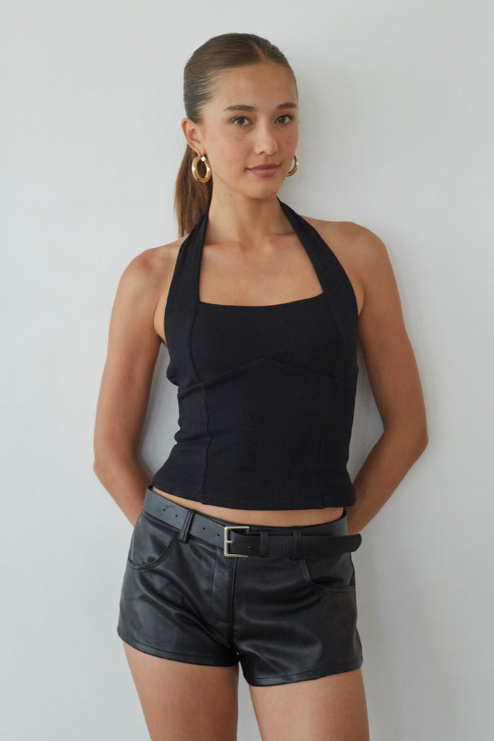 Woman wearing a black halter top and leather shorts against a plain background