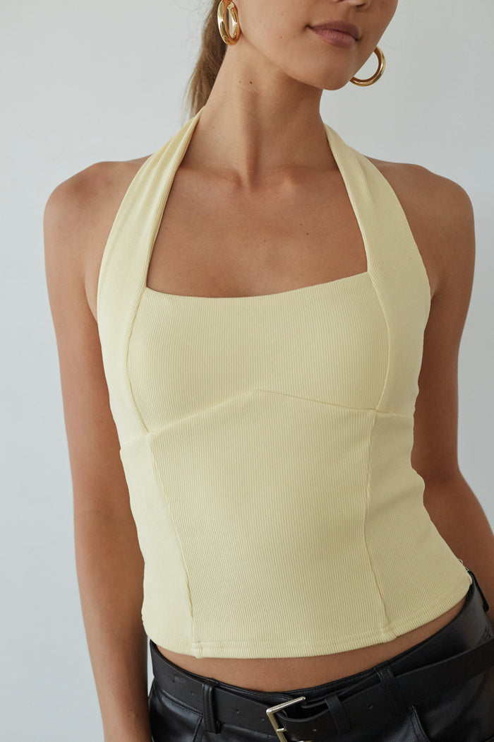 Woman wearing a light yellow halter top against a plain background