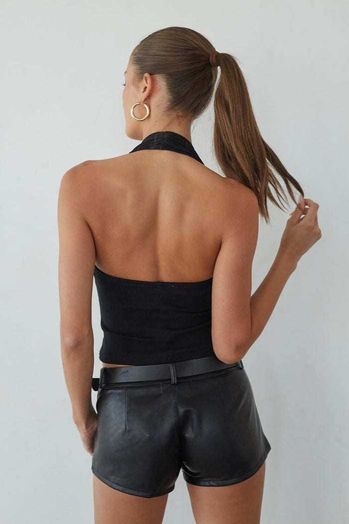 Woman wearing a black halter top and leather shorts against a plain background