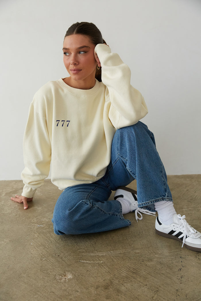 sitting view | butter yellow cozy crewneck that says The Lucky Club in Cobalt Blue with 777 Pocket detail
