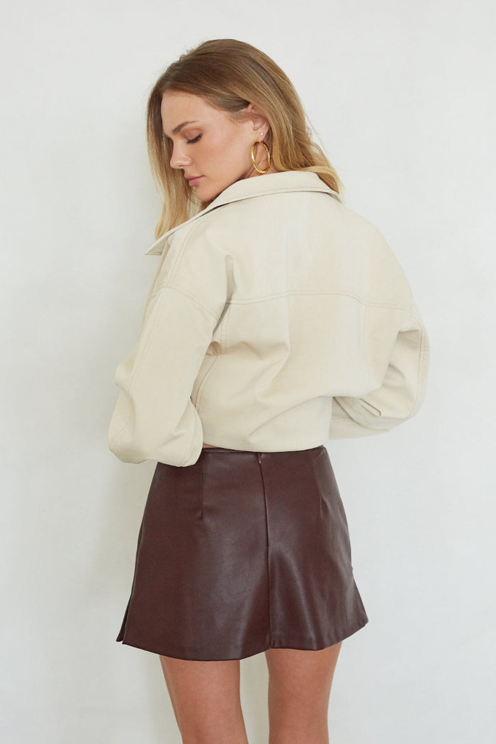 Woman wearing a cream jacket and brown leather skirt against a white background