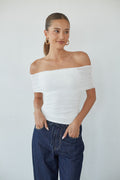 white-image | Woman wearing a white off-shoulder top and blue jeans against a plain background