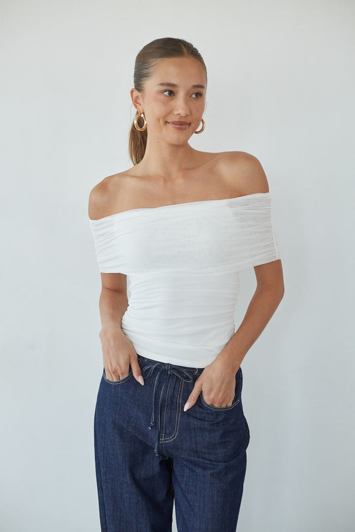white-image | Woman wearing a white off-shoulder top and blue jeans against a plain background