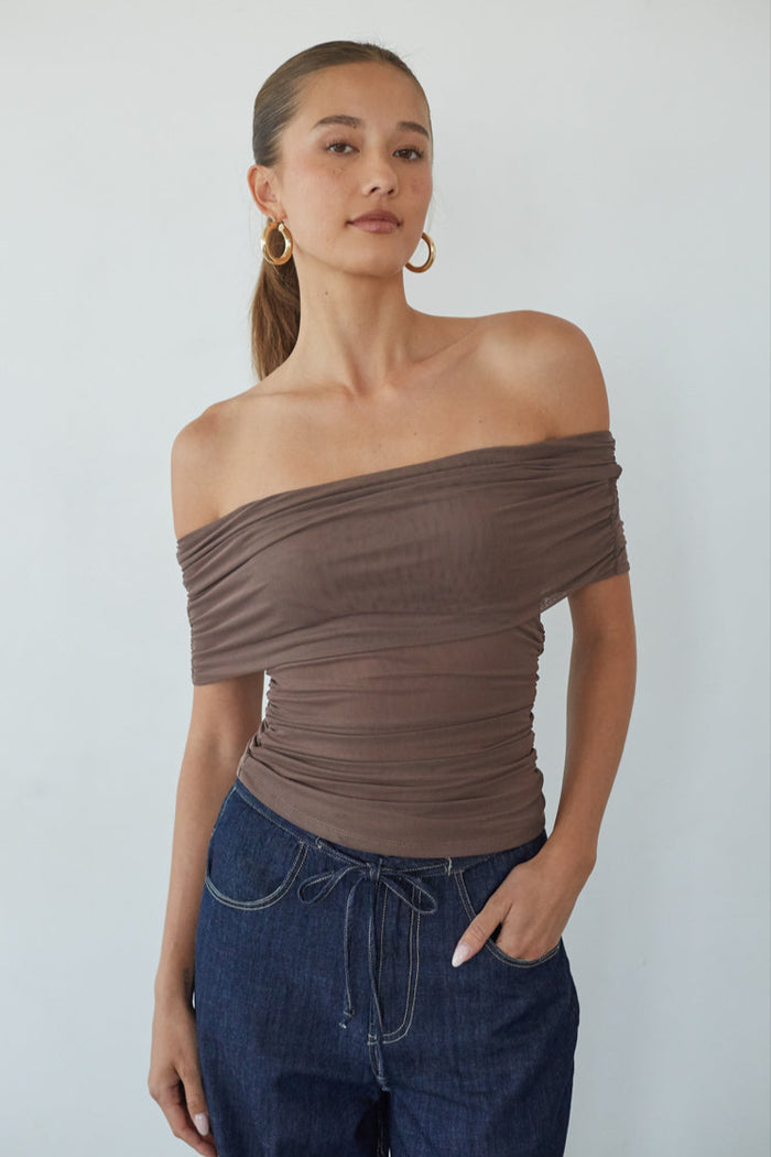 Woman wearing a brown off-shoulder top and blue jeans against a white background