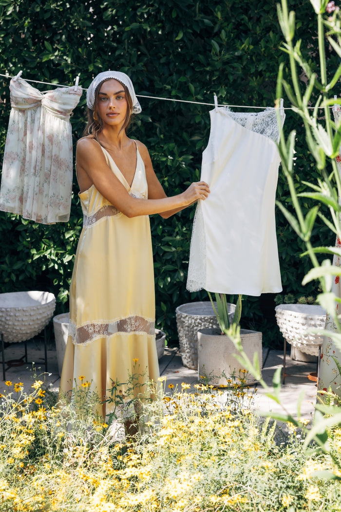 Woman hanging clothes on a line outdoors with greenery and flowers in the foreground