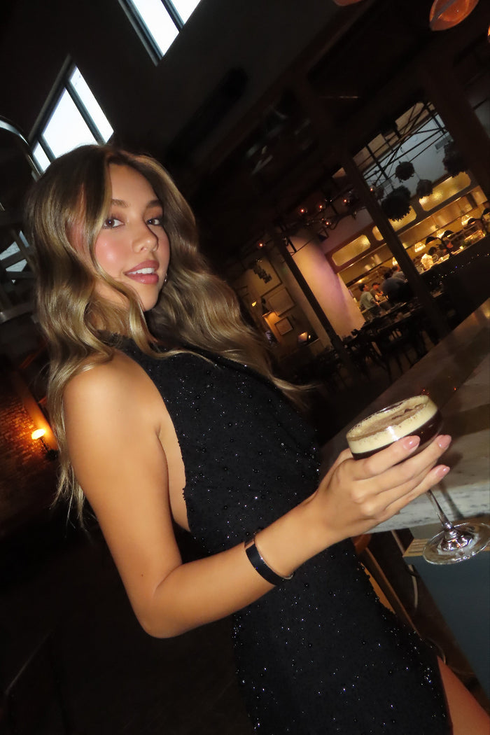 girl in a black embellished mini dress standing at the bar with a drink
