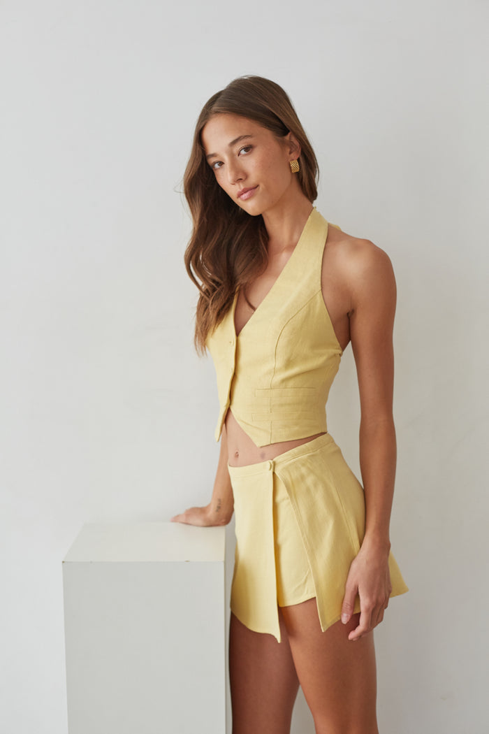 Side-image | Wrap Linen Mini Skort | side view highlighting the wraparound design and the structured waistline of the yellow skort.
