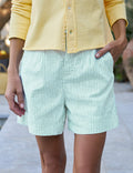 Person wearing light green striped shorts and a yellow shirt with a blurred background