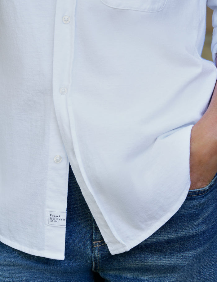 Close-up of a person wearing a white button-up shirt tucked into blue jeans, with the shirt pocket and front buttons visible.