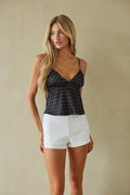 Woman wearing a black polka dot top and white shorts against a beige background