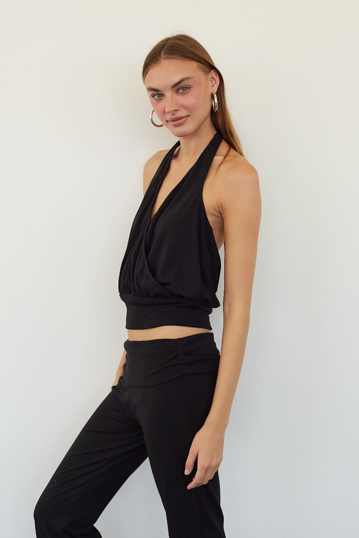 A woman modeling a black halter crop top and matching black high-waisted pants against a plain white studio background.