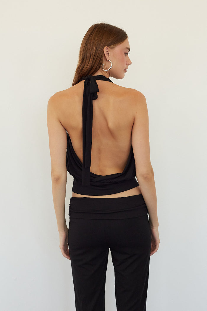 A woman shown from the back wearing a black halter-style open-back crop top and black pants against a plain light background.
