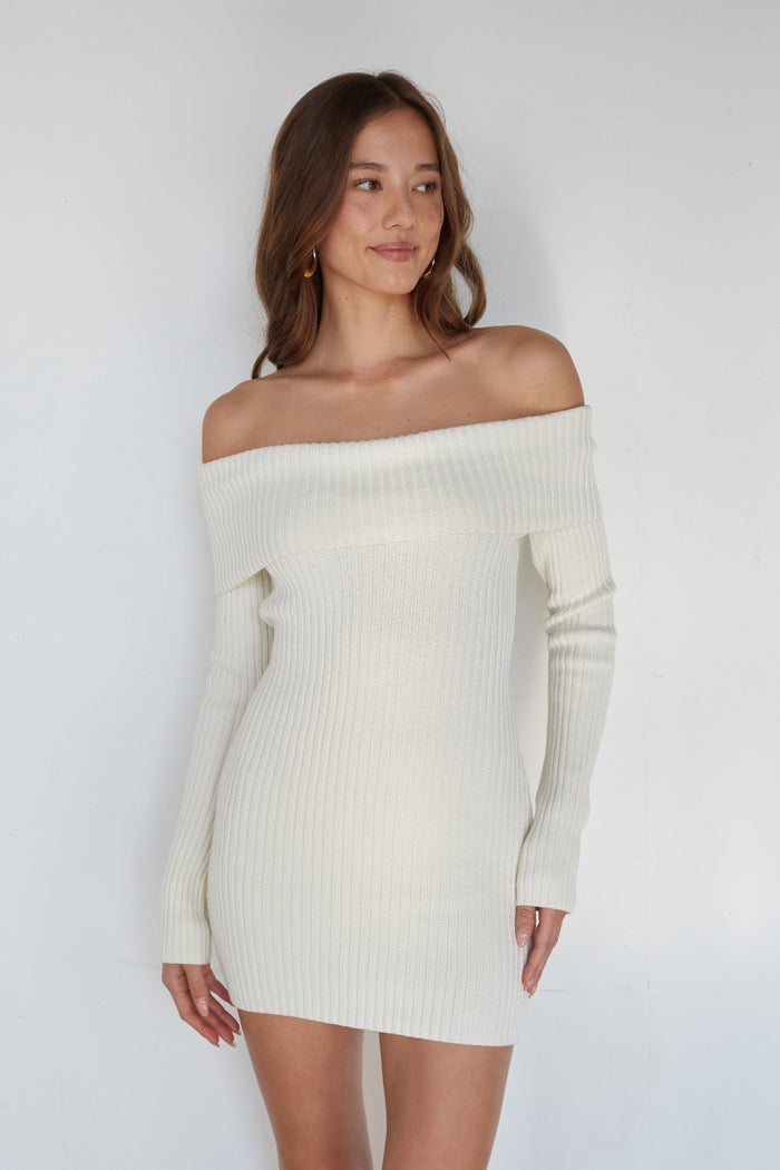 Woman wearing a white off-shoulder ribbed sweater dress against a plain background