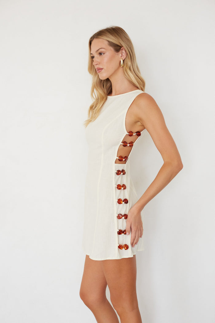 Woman wearing a white dress with red buttons on a plain background